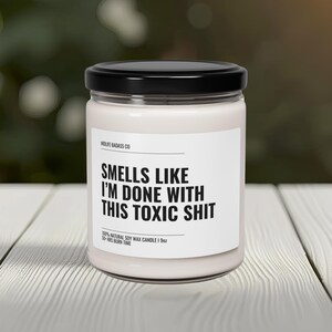 May include: A white candle with a black label that reads "Smells Like I'm Done With This Toxic Shit". The candle is made with 100% natural soy wax and has a 50-hour burn time.
