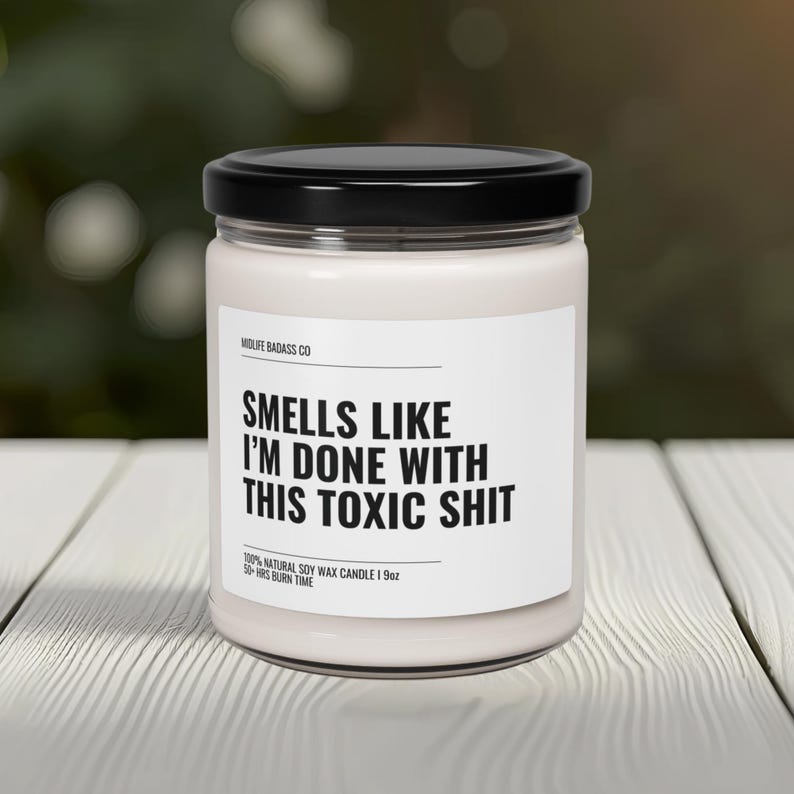 May include: A white candle with a black label that reads "Smells Like I'm Done With This Toxic Shit". The candle is made with 100% natural soy wax and has a 50-hour burn time.