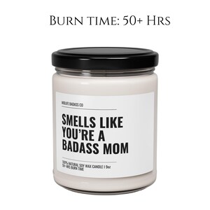 May include: A white candle jar with a black lid and label. The label reads "Smells Like You're A Badass Mom" and "100% Natural Soy Wax Candle | 9oz | 50+ Hrs Burn Time".