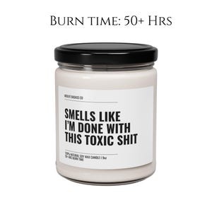 May include: A white candle jar with a black lid and label. The label reads "Smells Like I'm Done With This Toxic Shit" and "Midlife Badass Co". The candle is 100% natural soy wax and has a burn time of 50+ hours.
