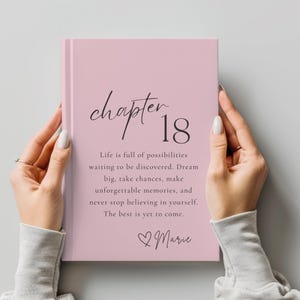 Peut inclure: Un livre à couverture rigide rose clair avec le texte "chapter 18" en police noire. En dessous, il est écrit : "Life is full of possibilities waiting to be discovered. Dream big, take chances, make unforgettable memories, and never stop believing in yourself. The best is yet to come." Une icône de cœur et le nom "Marie" sont imprimés en bas.