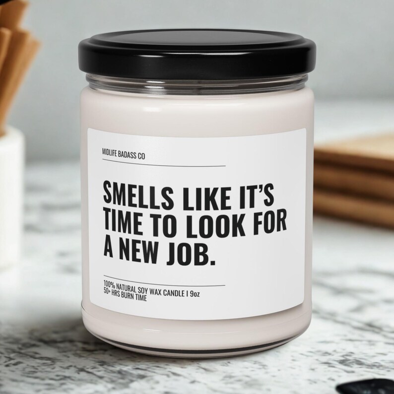 Pode incluir: Uma vela branca num frasco de vidro com tampa preta. O r&oacute;tulo diz "SMELLS LIKE IT'S TIME TO LOOK FOR A NEW JOB." &Eacute; uma vela de cera de soja natural de 255g com um tempo de queima de mais de 50 horas.