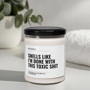 May include: A white soy wax candle with a black lid and label that reads "MOUFE BADASS CO" and "SMELLS LIKE I'M DONE WITH THIS TOXIC SHIT". The candle is 100% natural soy wax and has a 50-hour burn time.