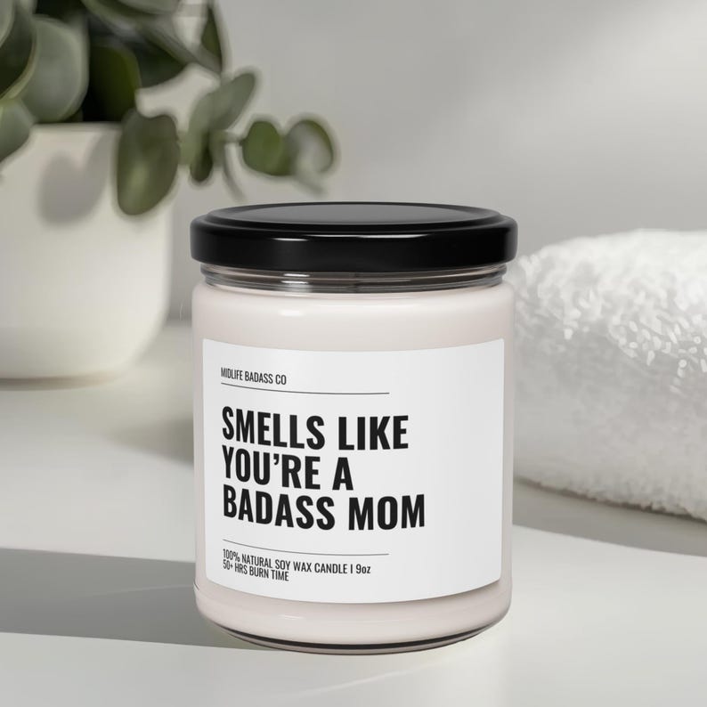 May include: A white candle with a black lid and label that reads "Smells Like You're A Badass Mom". The candle is made with 100% natural soy wax and has a burn time of 50 hours.