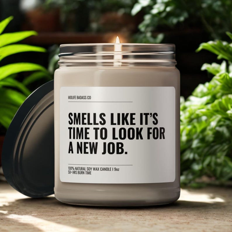 Pode incluir: Uma vela de cera de soja acesa num frasco de vidro com tampa preta. O r&oacute;tulo diz "SMELLS LIKE IT'S TIME TO LOOK FOR A NEW JOB." A vela tem 255g e um tempo de queima de 50 horas.
