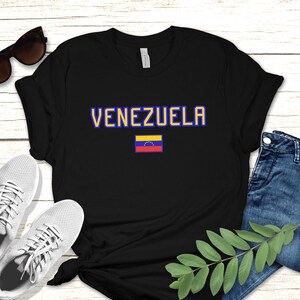 May include: Black t-shirt with the word "VENEZUELA" in blue and yellow letters and the Venezuelan flag printed on the front.