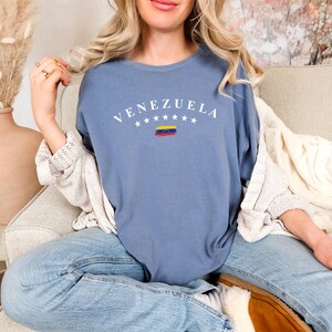 Pode incluir: Uma camiseta azul com a palavra "VENEZUELA" em letras brancas e um pequeno gr&aacute;fico da bandeira venezuelana.