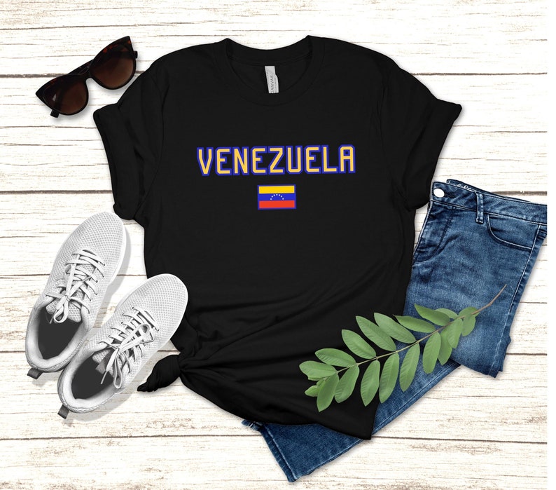 May include: Black t-shirt with the word "VENEZUELA" in blue and yellow letters and the Venezuelan flag printed on the front.