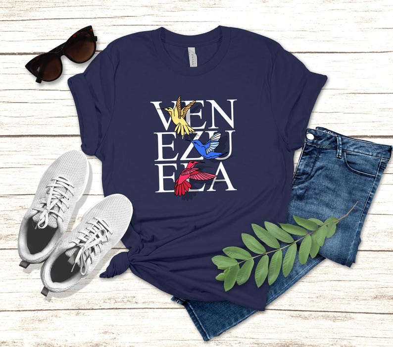 May include: A navy blue t-shirt with a white graphic of the word "VENEZUELA" with colorful hummingbirds flying around the letters.