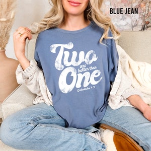 May include: A blue jean colored t-shirt featuring white distressed lettering that reads Two are better than One and Ecclesiastes 4:9. The shirt has a crew neckline and short sleeves, showcasing a vintage-inspired graphic print on the front chest.