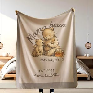 May include: A beige blanket featuring a Mama Bear and baby bear illustration with a honey pot. The blanket has the text "Mama bear", "Proverbs 31:10", "EST. 2021", and "Anna Isabella".