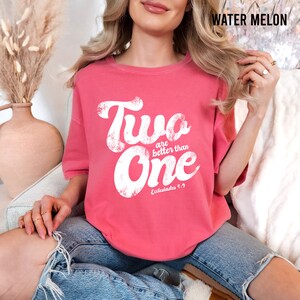 May include: A watermelon-colored t-shirt featuring white distressed text that reads Two are better than One and includes the reference Ecclesiastes 4:9. The shirt has a crew neckline and short sleeves, with the color name Water Melon printed in the corner.