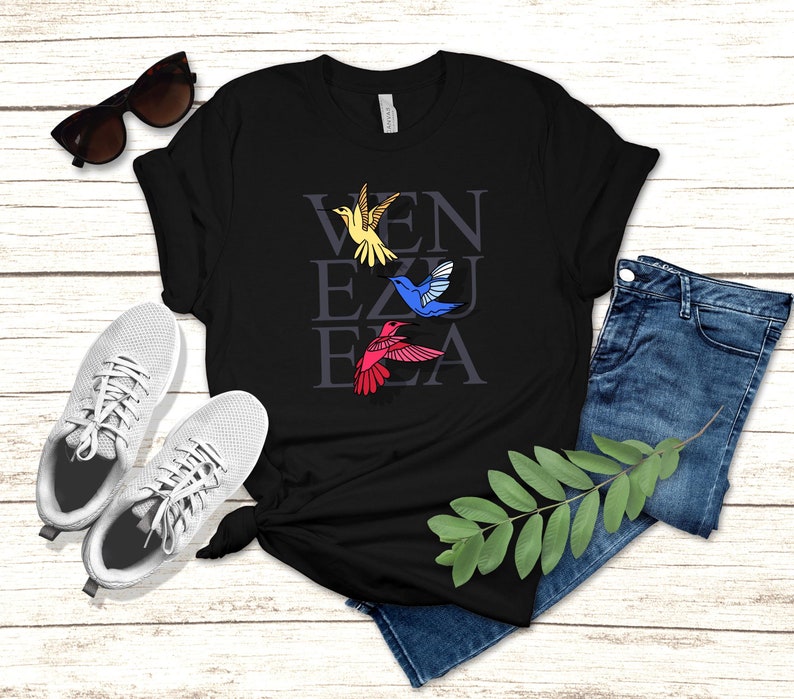 May include: Black t-shirt with the word "VENEZUELA" written in white letters with a yellow, blue, and red hummingbird flying above each letter.