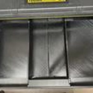 May include: A black and grey metal toolbox with a yellow handle and accents. The toolbox features a sliding tray and multiple compartments for organising tools. The interior is lined with a textured material.