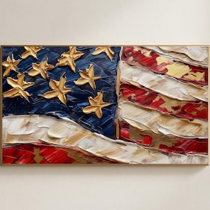 Könnte beinhalten: Texturierte Ölgemälde der amerikanischen Flagge in einem goldenen Rahmen. Die Flagge zeigt goldene Sterne auf blauem Grund und rot-weiße Streifen. Die dicken Pinselstriche erzeugen einen dreidimensionalen Effekt.