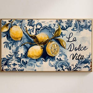Könnte beinhalten: Gerahmtes rechteckiges Kunstwerk mit gelben Zitronen an einem Zweig mit grünen Blättern. Der Hintergrund ist ein blau-weißes Blumenmuster. Der Schriftzug "La Dolce Vita" ist kursiv geschrieben.