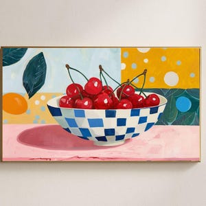 Könnte beinhalten: Gerahmtes Gemälde mit einer Schale voller Kirschen. Die Kirschen sind leuchtend rot und liegen in einer blau-weiß karierten Schale. Der Hintergrund ist ein farbenfroher Patchwork aus Gelb, Blau und Rosa. Das Gemälde hat einen goldenen Rahmen.
