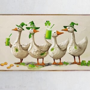 Könnte beinhalten: Gerahmtes Gemälde mit vier weißen Gänsen, die den St. Patrick's Day feiern. Jede Gans trägt einen grünen Hut und hält ein grünes Getränk. Goldmünzen und Kleeblätter sind um die Gänse verstreut.