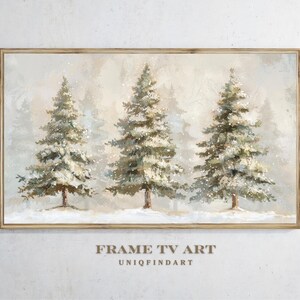Könnte beinhalten: Gerahmtes Gemälde mit drei schneebedeckten Tannen in einer winterlichen Waldszene. Das Kunstwerk hat eine neutrale Farbpalette mit einem hellbraunen Holzrahmen. Der Text "FRAME TV ART" und "UNIOFINDART" befindet sich unten.