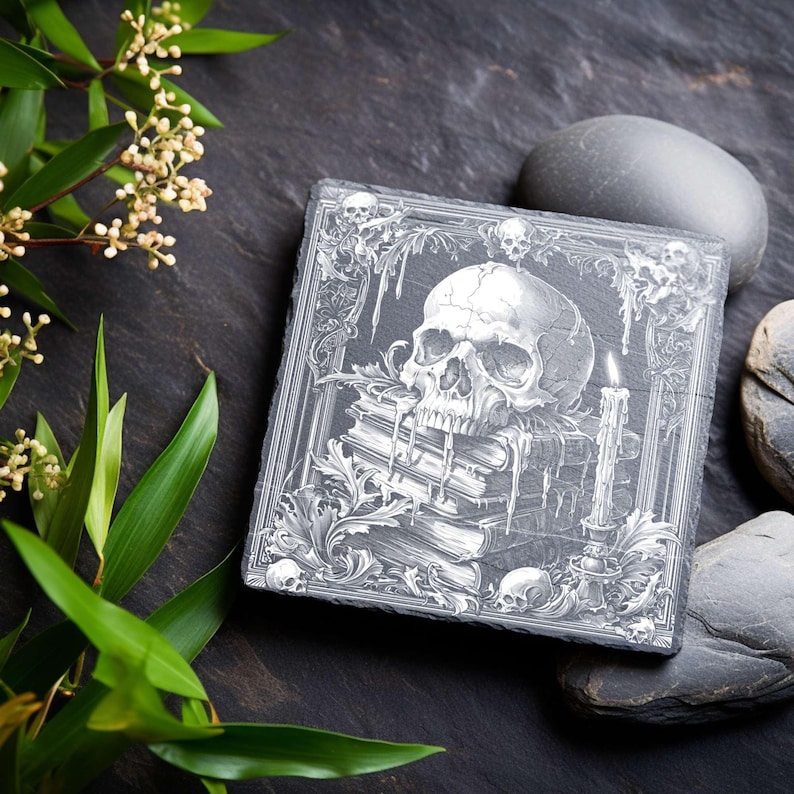 May include: Square, dark gray slate coaster with a detailed, engraved design. The design features a skull atop a stack of books, a lit candle, and decorative borders. The coaster is a unique home decor item.