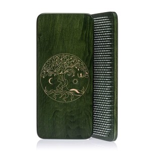 May include: A green wooden comb with a tree of life design. The comb has a dark green finish and an engraved tree motif with a moon and sun. The comb's teeth are visible on the side.
