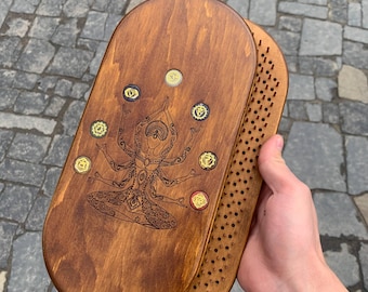 Könnte beinhalten: Ein Meditationsbrett aus Holz mit dunkelbraunem Finish. Das Brett zeigt ein detailliertes geätztes Design einer Figur mit mehreren Armen und kreisförmigen Akzenten. Das Brett ist oval geformt und hat auf einer Seite kleine Löcher.