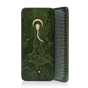 May include: A green wooden comb with a detailed illustration of a woman with outstretched arms, a crescent moon, and stars. The comb's teeth are visible on the right side. The design is in a light tan color, contrasting with the dark green background.