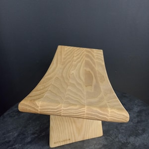 May include: A light-colored wooden display stand with a curved top and a rectangular base. The wood grain is visible, and the stand is likely for displaying items. The base has the text "METACRAFT" on it.