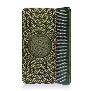 May include: A wooden hair comb with a decorative design. The comb features a dark green colour with a geometric pattern and a central mandala design. The comb's teeth are visible on the right side.