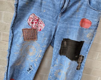 May include: Blue denim jeans with patchwork details, including floral fabric, plaid, and mesh. The jeans have a distressed look and feature a lace trim at the bottom.