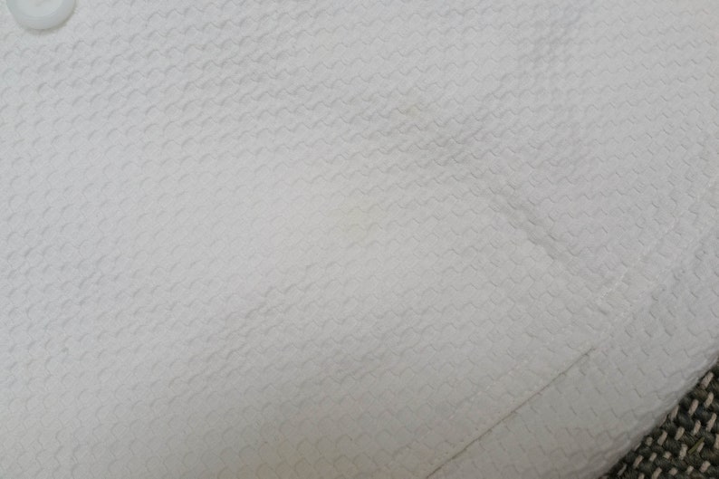 May include: White fabric with a textured, woven pattern. The fabric has a subtle sheen and a smooth, soft feel.