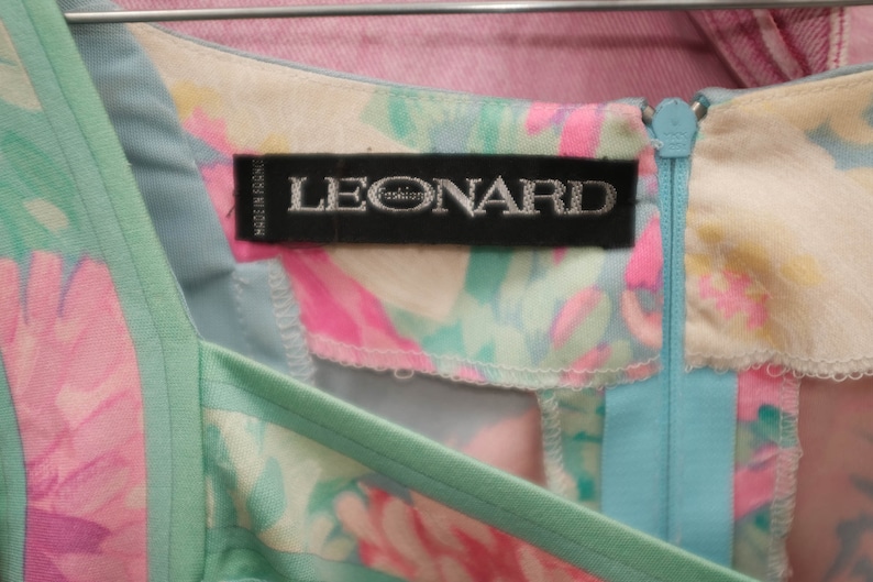 May include: A light blue and pink floral dress with a green trim and a zipper closure. The dress has a label that reads "LEONARD Paris".
