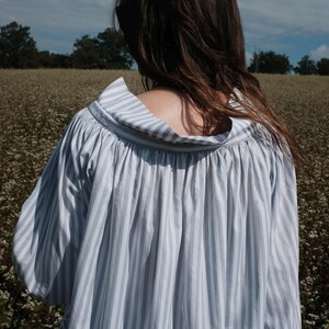 May include: A white and blue striped shirt with a loose, flowing fit and a gathered neckline. The shirt is made of a lightweight fabric and has a relaxed, casual style.