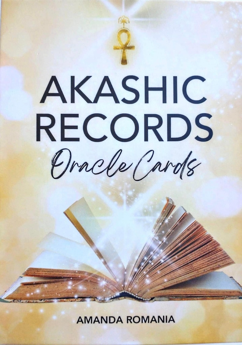 Pu&ograve; includere: Un mazzo di carte Oracle Akashic Records con un simbolo Ankh dorato e un libro aperto con una luce brillante che ne emana. Il testo sulla carta recita "Akashic Records Oracle Cards" e "Amanda Romania".