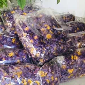 May include: Several clear plastic bags filled with dried purple and yellow flowers. The bags are arranged in a pile on a tiled floor.