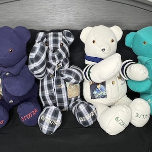 May include: Four teddy bears made from repurposed clothing. The bears are wearing a blue shirt, a plaid shirt, a white shirt, and a teal shirt. Each bear has a date embroidered on its paw.
