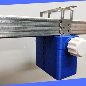 May include: A blue plastic device with a white knob and numbers 1 through 10 printed on the side. The device is hanging from a metal track.