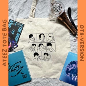 Könnte beinhalten: Eine weiße Canvas-Tragetasche mit schwarzen Linienzeichnungen von acht Personen. Die Tragetasche hat einen schwarzen Griff und die Worte "ATEEZ TOTE BAG" sind vertikal auf der linken Seite der Tasche aufgedruckt. Die Worte "OT8-VERSION" sind vertikal auf der rechten Seite der Tasche aufgedruckt.
