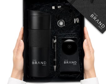 Könnte beinhalten: Eine schwarze Geschenkbox mit einem mattschwarzen Reisebecher mit strukturierter Grifffläche, einem schwarzen Kugelschreiber, einer kabellosen Ladestation und einem Kabelset. Jeder Artikel trägt den Text YOUR BRAND HERE. Der Deckel ist schwarz mit Schleife.