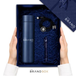 K&ouml;nnte beinhalten: Eine dunkelblaue Geschenkbox mit einer zylindrischen, dunkelblauen Isolierflasche mit dem Text YOUR BRAND HERE, einem schwarzen Multi-Port-Ladekabel mit rundem YOUR LOGO HERE-Anh&auml;nger und einem dunkelblauen Kugelschreiber mit YOUR LOGO HERE.