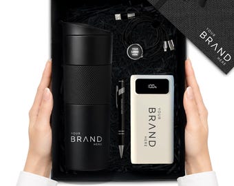Könnte beinhalten: Eine schwarze Geschenkbox mit einem schwarzen Reisebecher mit strukturierter Grifffläche, einer weißen Powerbank mit digitaler 100%-Anzeige, einem schwarzen Kugelschreiber und einem schwarzen Ladekabel mit Logo-Anhänger. Alle tragen den Text YOUR BRAND HERE.