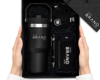 Könnte beinhalten: Eine schwarze Geschenkbox mit einem mattschwarzen Becher mit Henkel, einer schwarzen Powerbank mit Digitalanzeige bei 100 %, einem schwarzen Stift und einem schwarzen Ladekabel. Jeder Artikel trägt den weißen Schriftzug YOUR BRAND HERE.