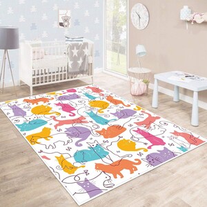 May include: A white area rug with a colorful cat pattern. The rug features a variety of cats in different colors and poses, including orange, pink, blue, purple, and yellow. The rug is perfect for a child's room or play area.