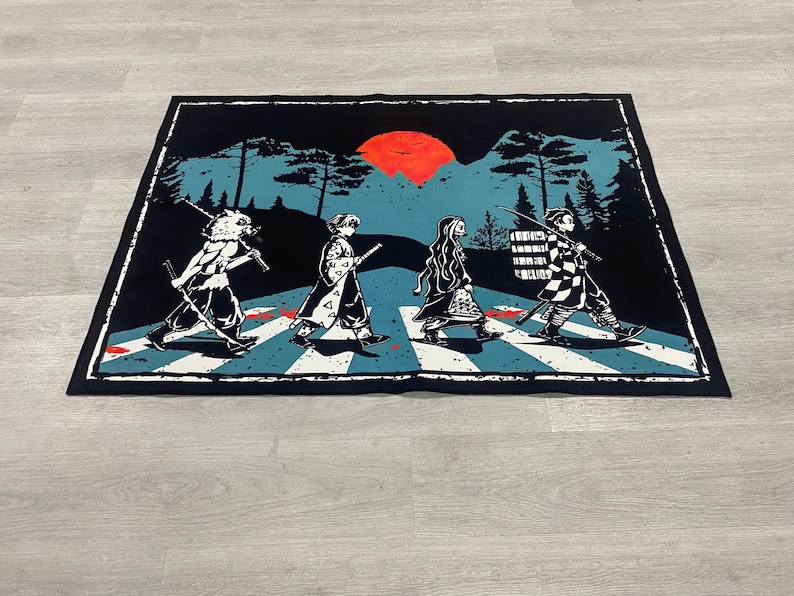 Puede incluir: Alfombra rectangular negra con una parodia de la portada del &aacute;lbum Abbey Road con personajes de la serie de anime Demon Slayer cruzando un paso de cebra. El fondo incluye un sol rojo, monta&ntilde;as y &aacute;rboles. La alfombra tiene un borde negro.