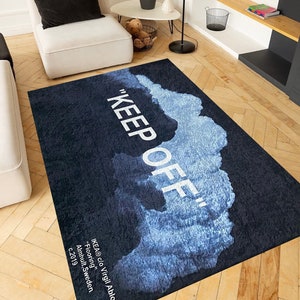 Può includere: Un tappeto nero e blu con il testo "KEEP OFF" in bianco. Il tappeto ha un design simile all'acquerello con nuvole blu su uno sfondo nero. Il testo "IKEA® c/o Virgil Abloh ™" è stampato in bianco nella parte inferiore del tappeto.