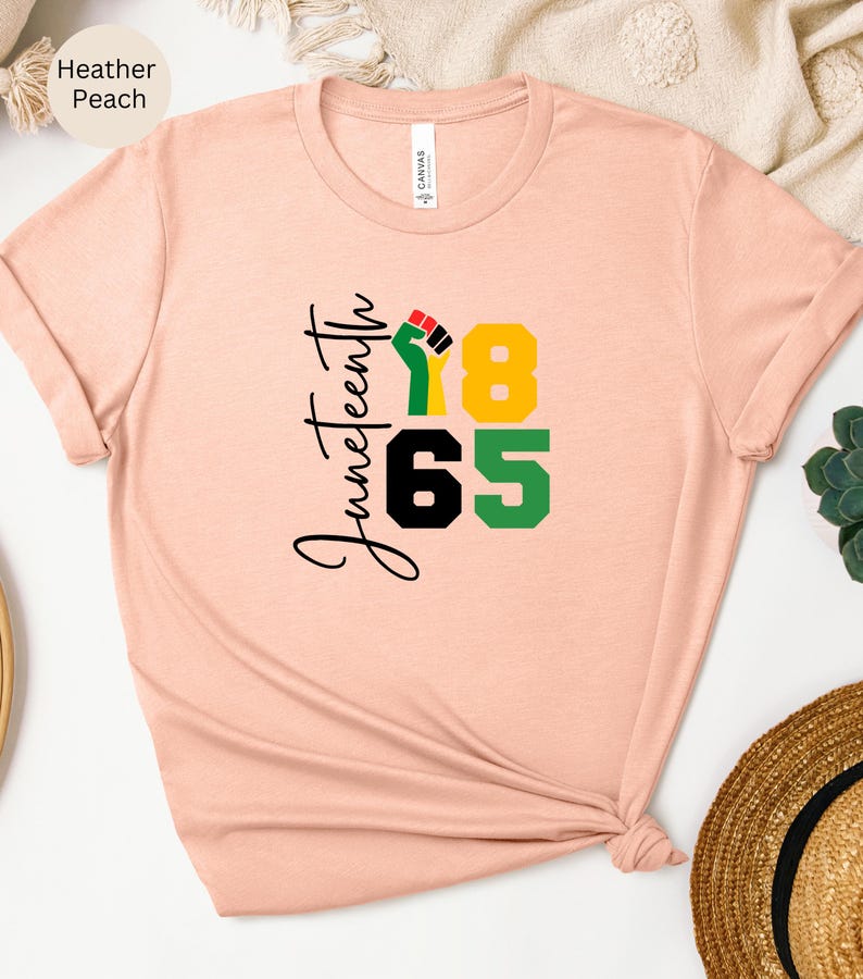 Puede incluir: Una camiseta de color melocot&oacute;n jaspeado con el texto "Juneteenth 1865" y un gr&aacute;fico de un pu&ntilde;o levantado en negro, rojo, verde y amarillo.