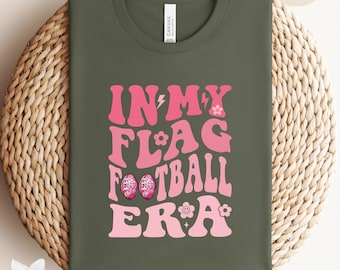 May include: A green t-shirt with the text "IN MY FLAG FOOTBALL ERA" in pink with a flower and lightning bolt design.