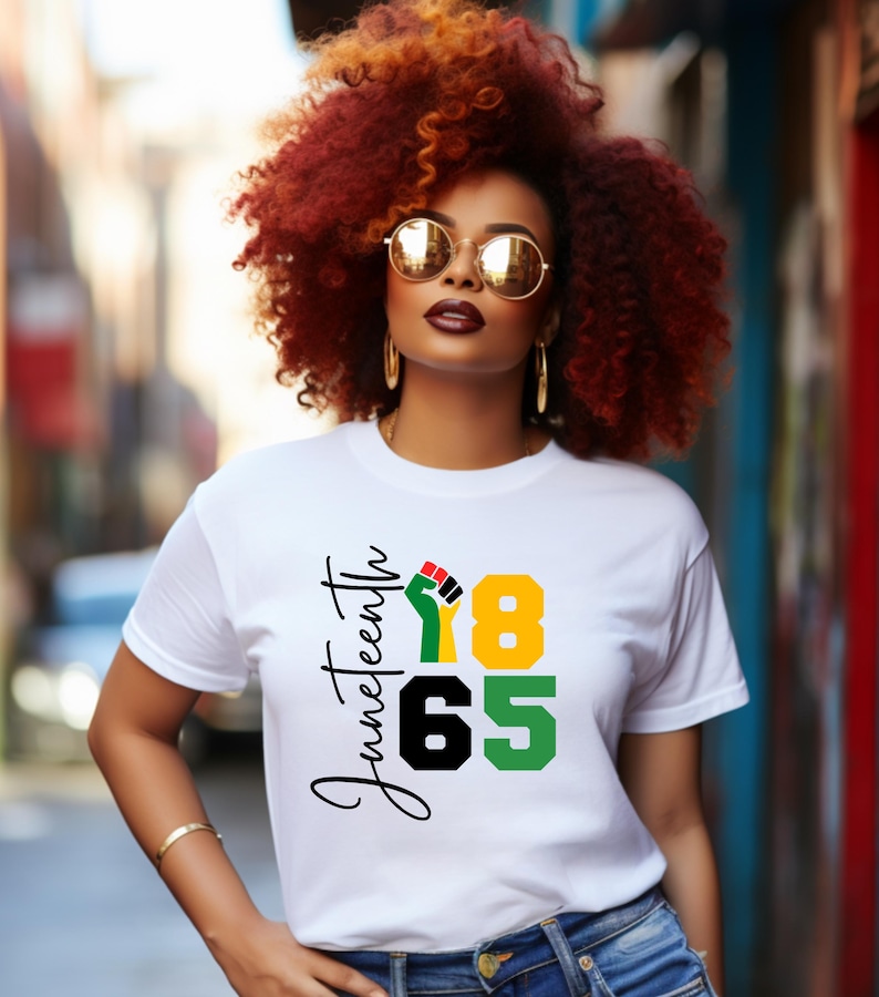 May include: A white t-shirt with black text that says 'Juneteenth 1865' and a black fist with red, yellow, and green colors.