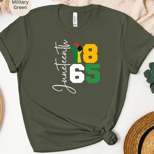 Puede incluir: Una camiseta verde con el texto "Juneteenth 1865" en blanco. Un pu&ntilde;o negro con acentos rojos, amarillos y verdes est&aacute; en el centro del dise&ntilde;o.