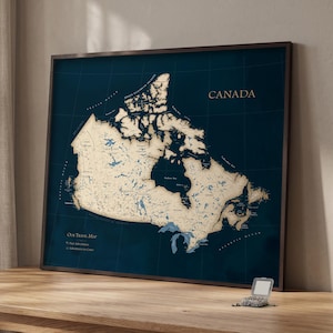 Puede incluir: Un mapa de pared enmarcado de Canadá con un fondo azul oscuro y una masa terrestre de color beige claro. El mapa muestra provincias, territorios y cuerpos de agua. El texto incluye "CANADA", "Our Travel Map", "Past Adventures" y "Adventures to Come".